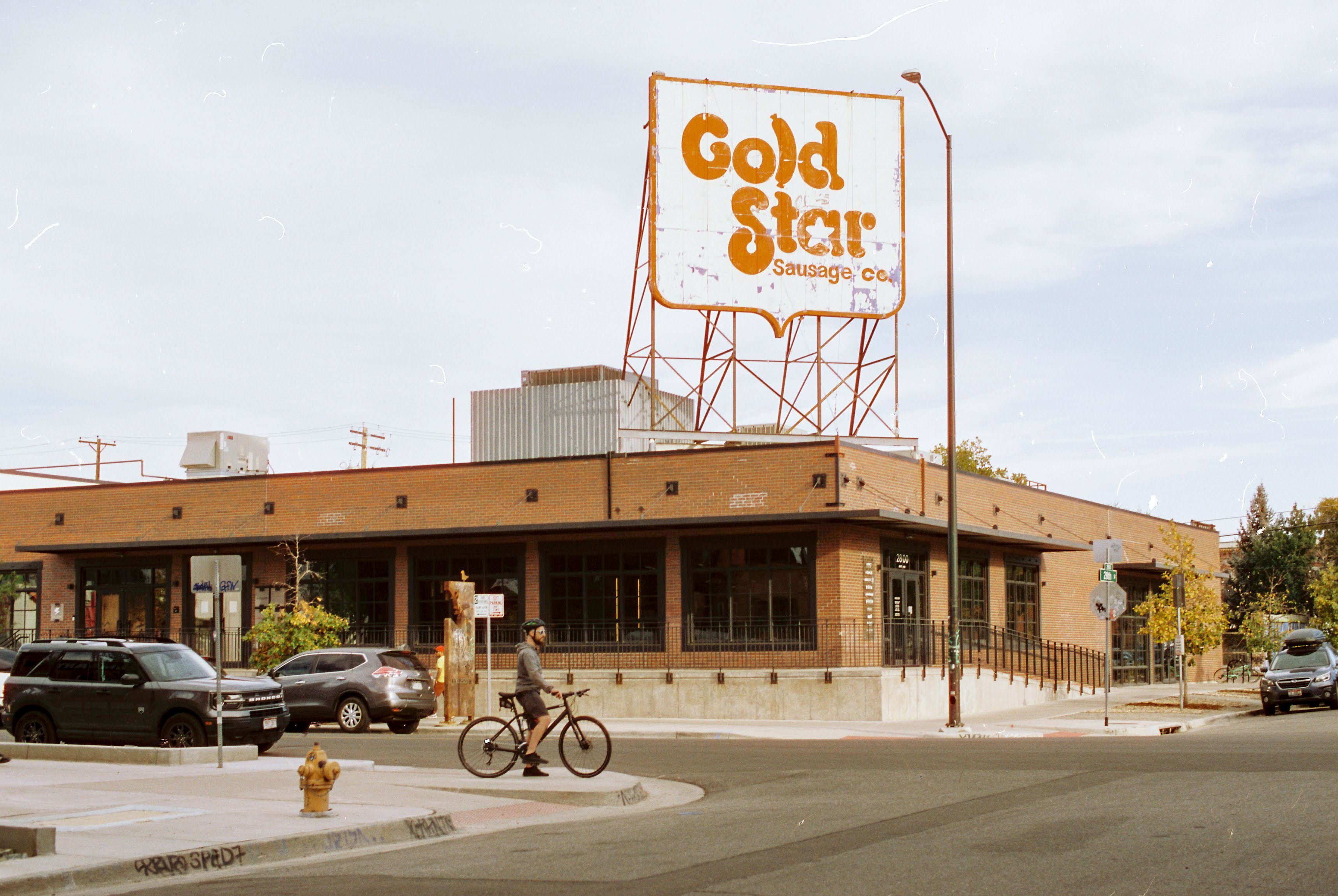 Gold Star Sausage Co. sign above a brick building in Denver's RiNo district, with a cyclist crossing the street below