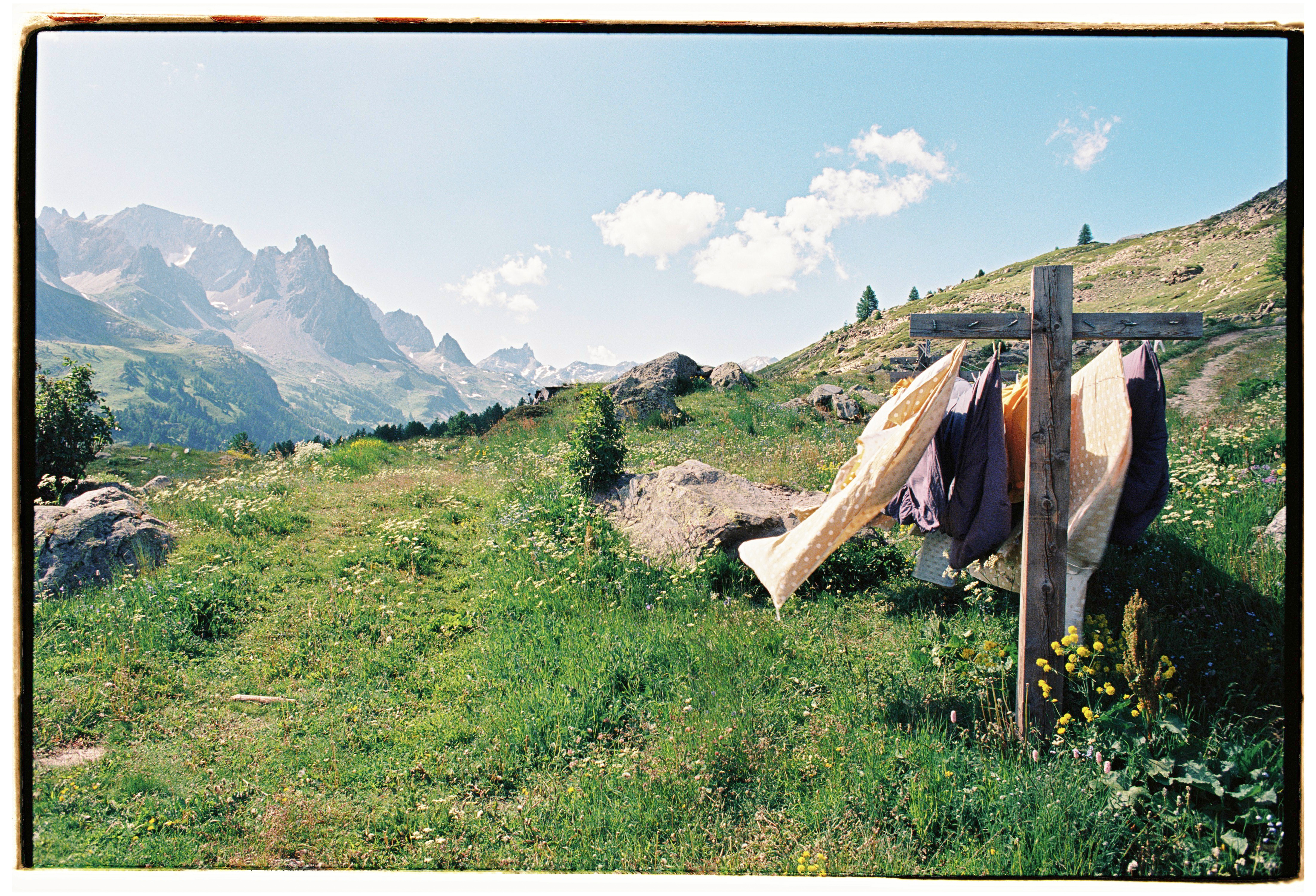 Clothes hanging from a wooden cross in an alpine meadow, with mountains behind them