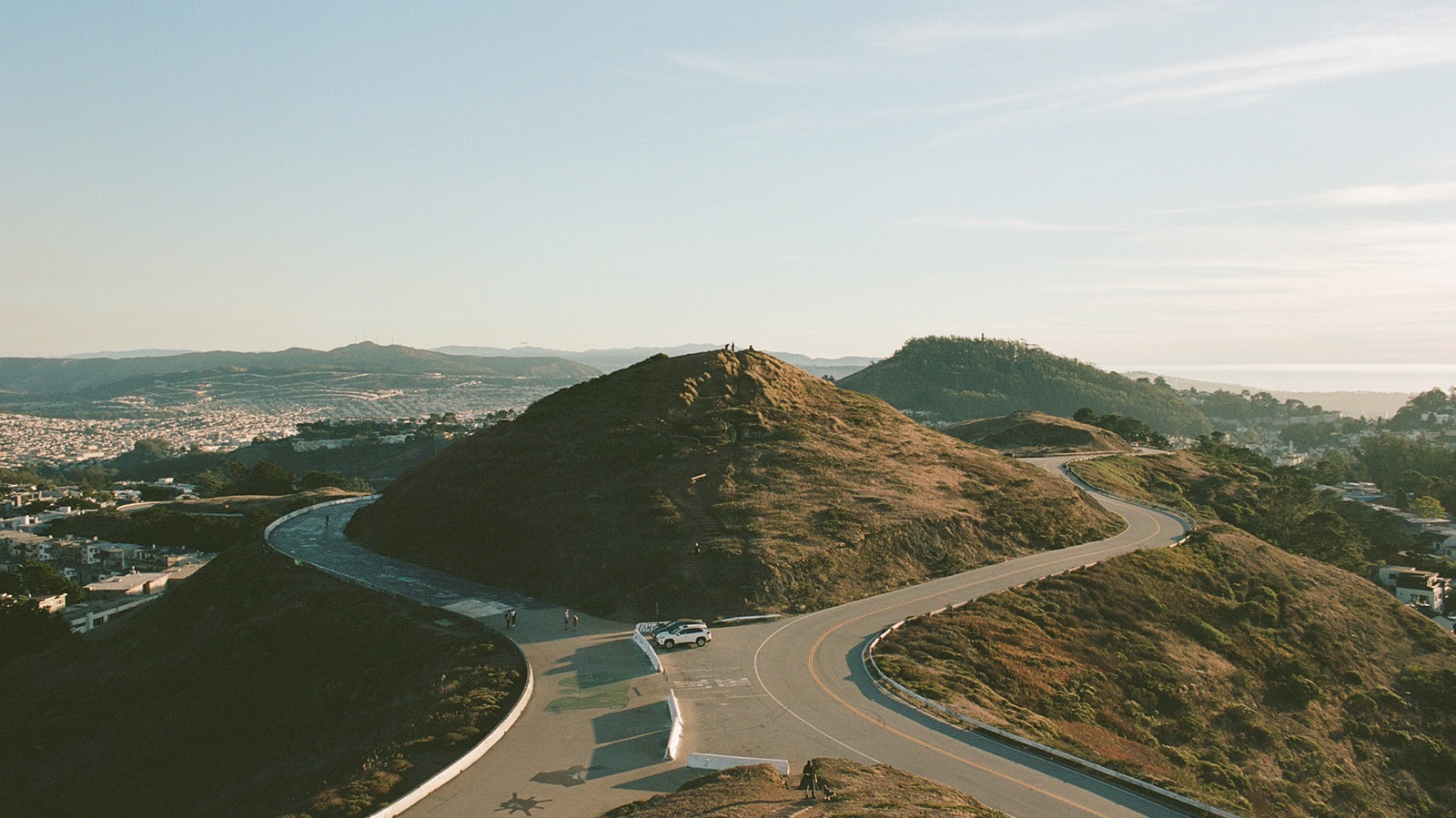 Twin Peaks at golden hour, two hills with winding roads between them and San Francisco sprawled below