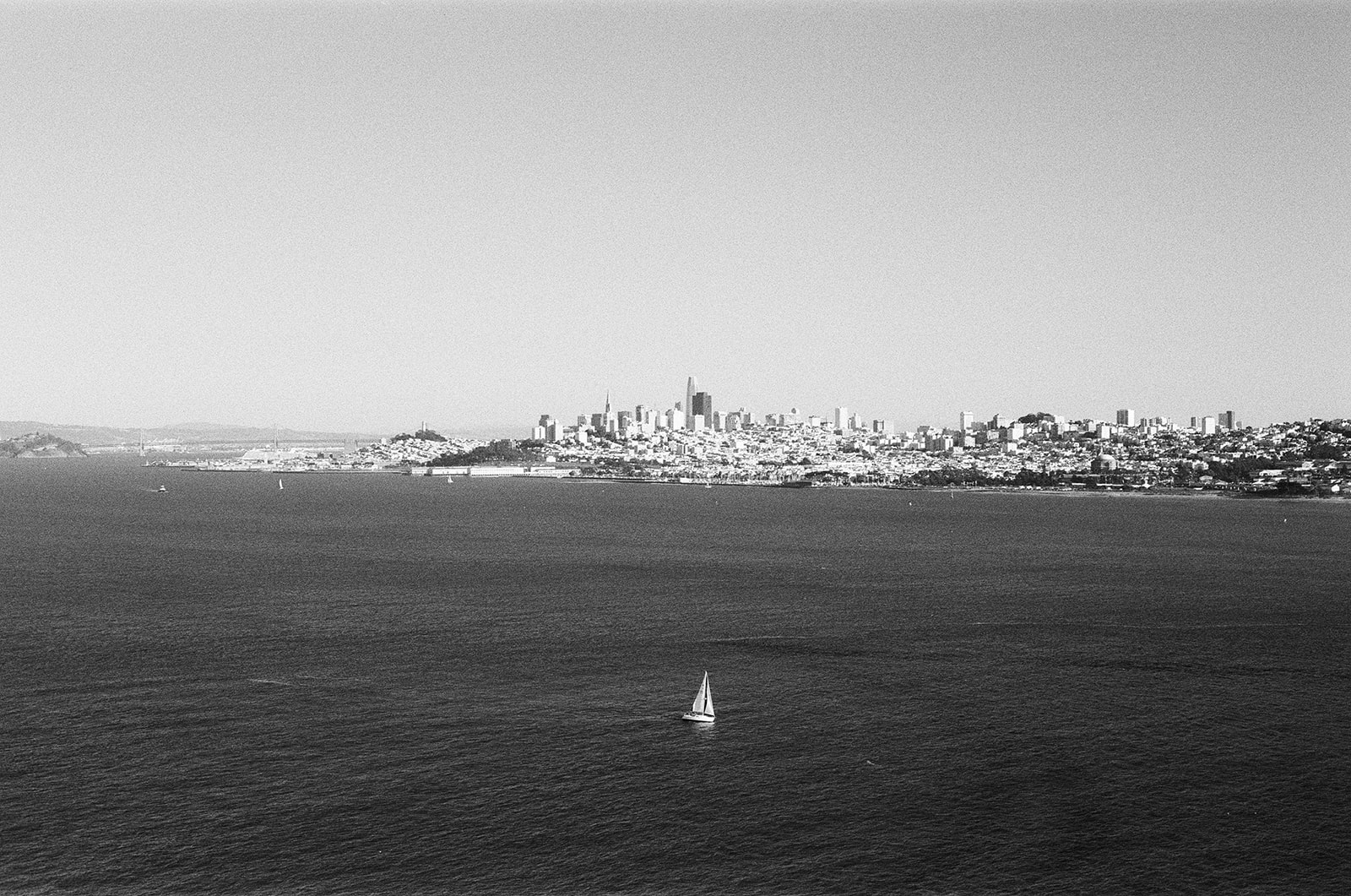 Black-and-white photograph of a sailboat on the bay, with San Francisco’s skyline in the distance